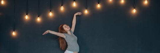 Junge, schwangere Frau tranzt glücklich unter vielen Glühbirnen